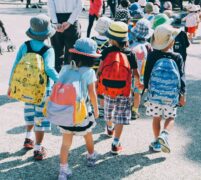 Children walking away from the camera. They are all wearing backbacks and hats.