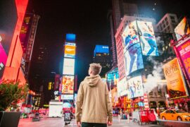 A teenage boy stares up at a multitude of ads designed to get his attention; some of which focus on hyper sexualization of the products being advertised.