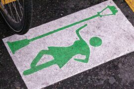 Painting on concrete symbolizing the profession known as prostitution. It is a woman in a short skirt painted in green, standing next to a green lamppost. The green is outlined in a white square.