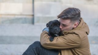 A treatment plan with dogs or horses can be helpful as in this photo of a man clinging tightly to his dog. The man is sittin on the ground outside, wearing a jacket, hugging his dog.