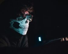 Anti-child sex trafficking initiatives include prevention helping keep children safe from online predators like one portrayed in this image of and adult in the dark looking at a computer screen, which is reflected in his glasses. He is wearing a mask depicting a skull.