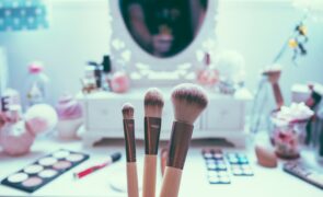 This photo shows the abundance of makeup products one might use to validate their self-worth through beauty products. Shown are makeup brushes, vanity mirror, lots of colored palettes, and other makeup items.